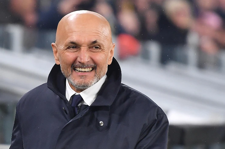 Luciano Spalletti sorride durante una partita, indossa un cappotto blu navy con sciarpa e cravatta