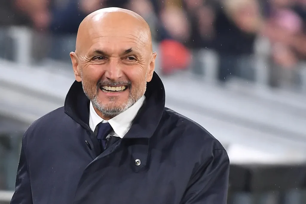 Luciano Spalletti sorride in panchina durante una partita, indossa un cappotto blu navy