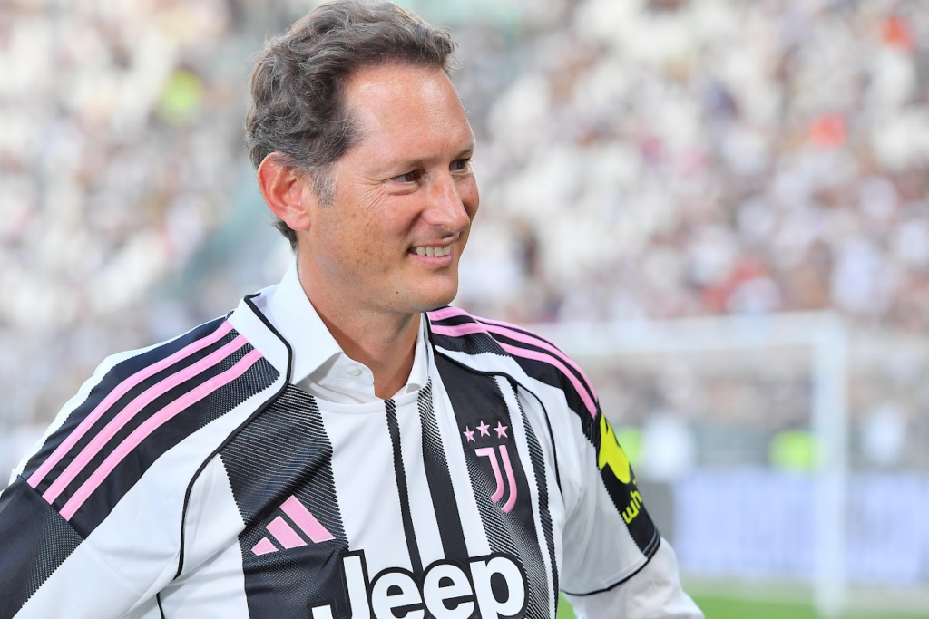 John Elkann con la maglia della Juventus a strisce rosa e nere, sorride durante un evento allo stadio