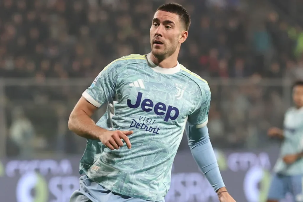 Dusan Vlahovic in maglia azzurra Juventus durante una partita, con fascia al braccio sinistro