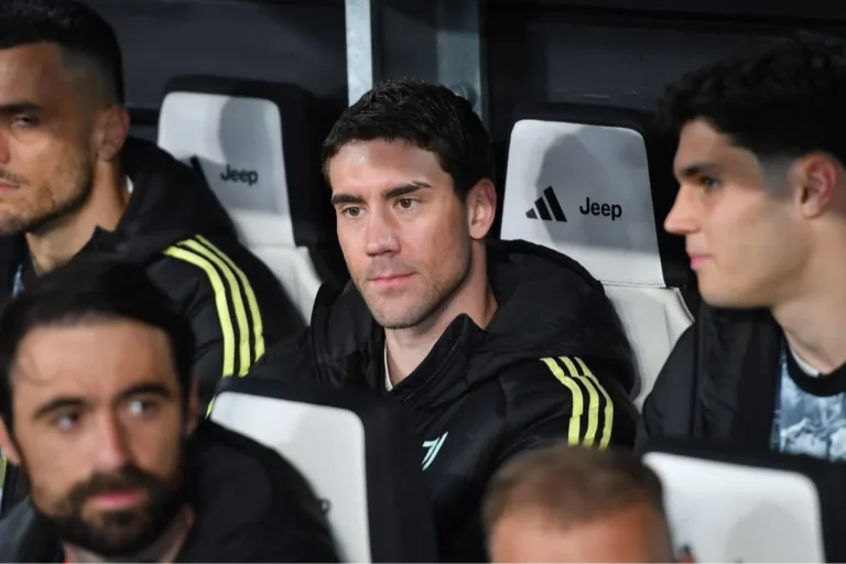 Dusan Vlahovic in panchina durante una partita della Juventus, in tuta Adidas nera con dettagli gialli