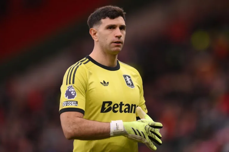 Dibu Martinez portiere con guanti gialli durante una partita, in divisa Adidas gialla con sponsor Betaim