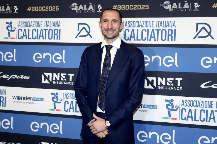 Giorgio Chiellini in abito blu scuro durante un evento ufficiale davanti al backdrop dell'Associazione Italiana Calciatori