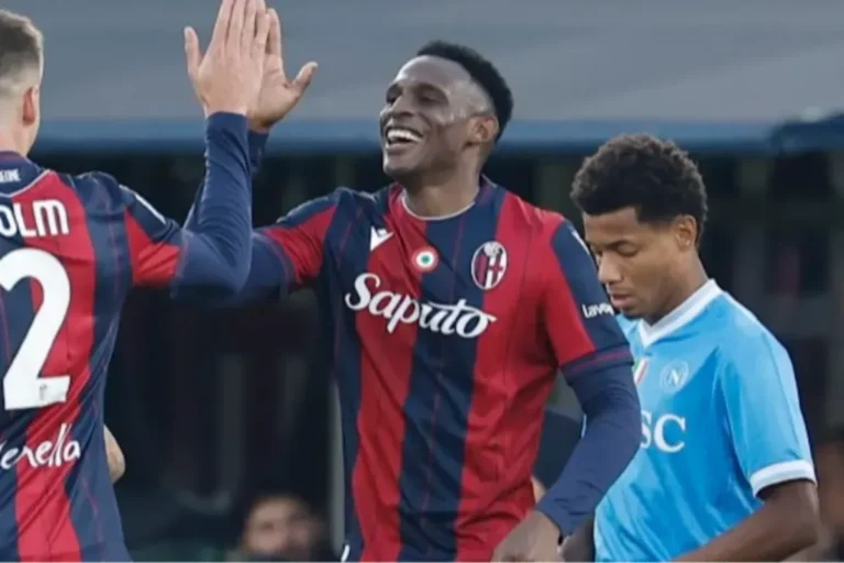 Lucumì esulta con i compagni durante una partita del Bologna, indossando la maglia a strisce rosse e blu