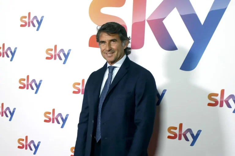 Giovanni Carnevali in abito scuro e cravatta davanti a uno sfondo con logo Sky