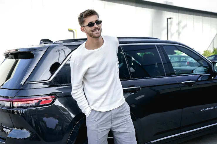 Guglielmo Vicario in arrivo alla Juventus, con maglia bianca e occhiali da sole, accanto a un SUV nero