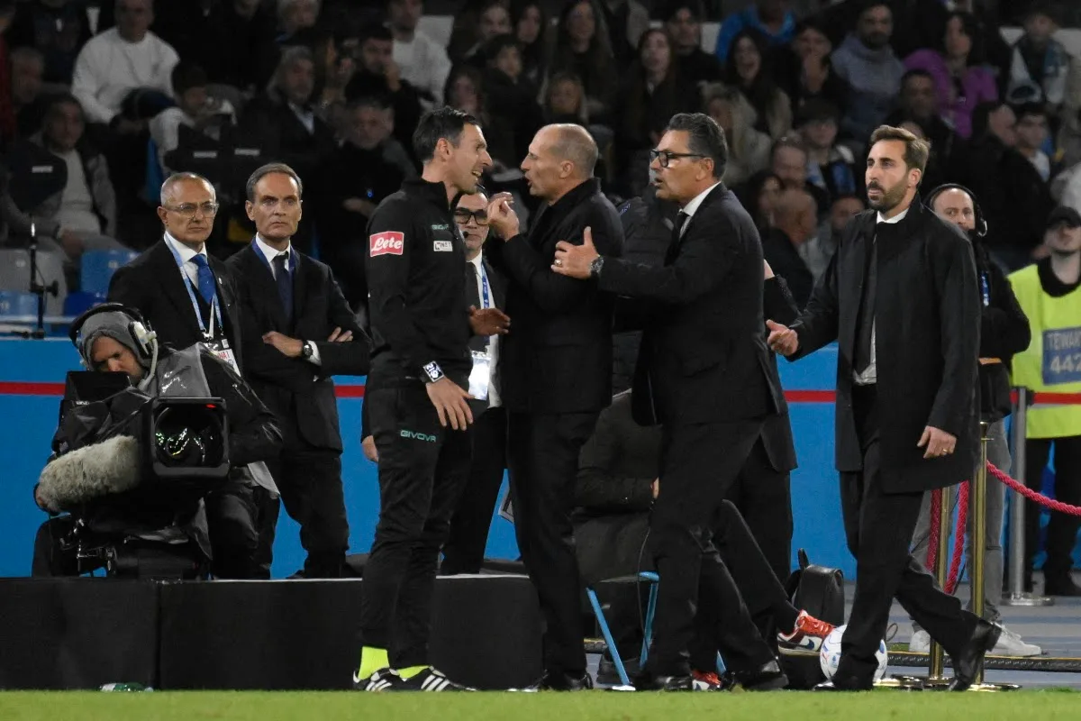 Confronto acceso a bordo campo tra un uomo in abito scuro e un arbitro in tuta nera durante una partita di calcio
