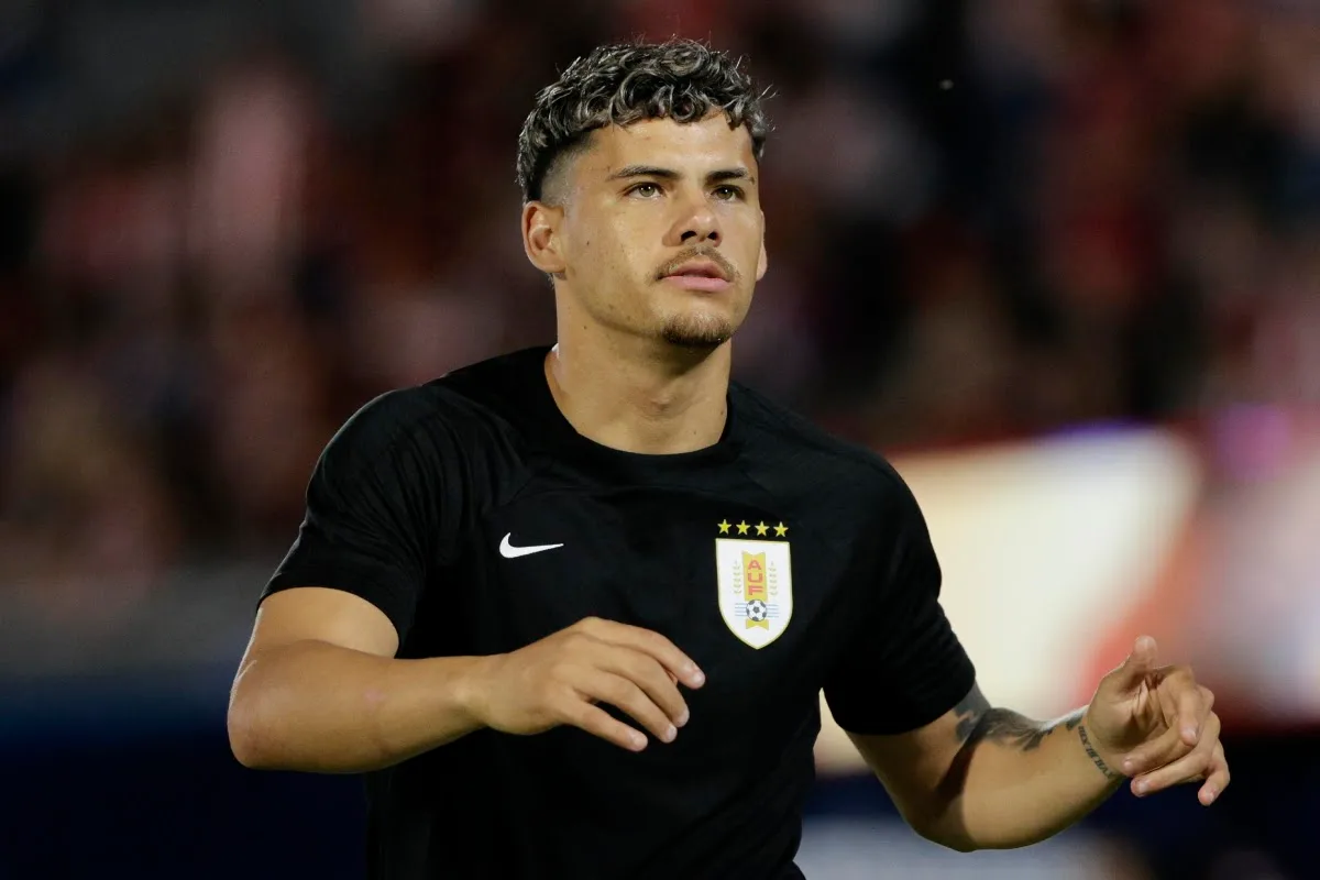 Calciatore con maglia nera Nike e stemma della nazionale dell'Uruguay, con sfondo sfocato di tifosi allo stadio
