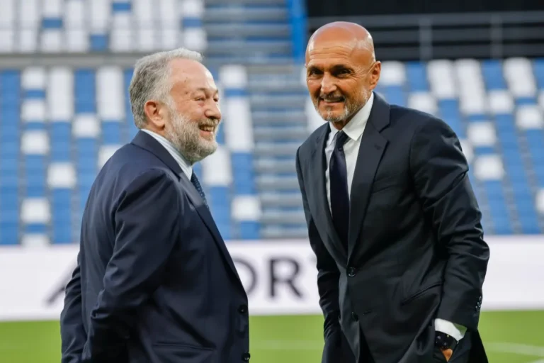 Gianluca Ferrero e Spalletti conversano su un campo da calcio, con tribune blu e bianche sullo sfondo