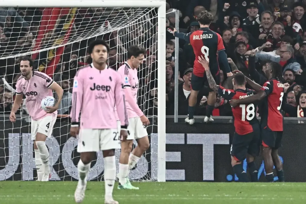 Giocatori della Juventus in maglia rosa delusi in primo piano mentre i giocatori del Genoa esultano sotto la curva rossoblù