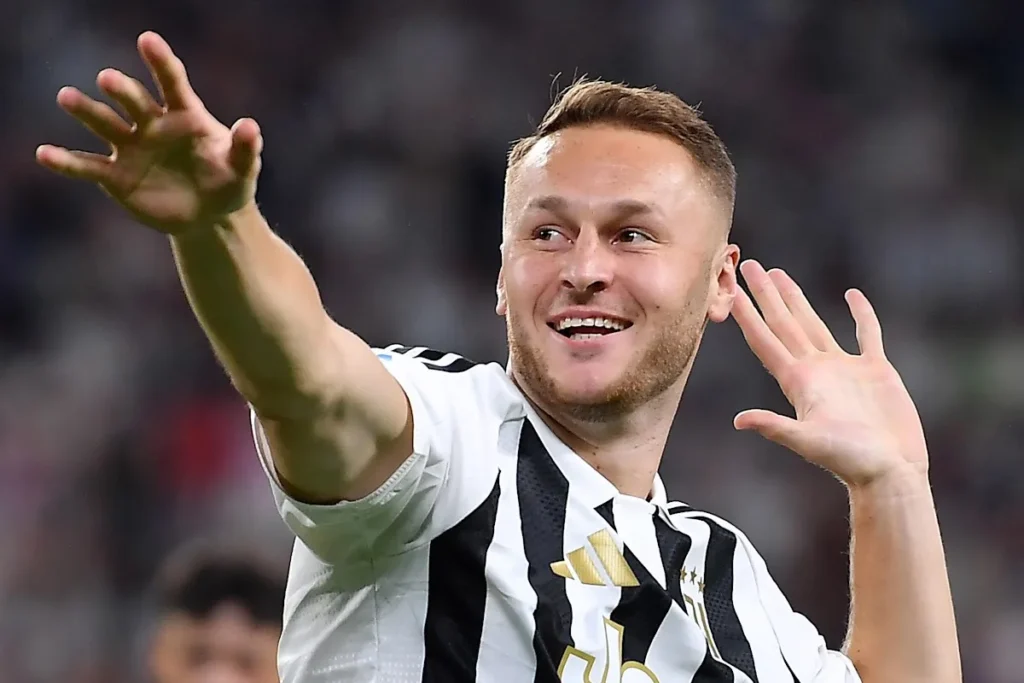 Calciatore della Juventus con maglia bianconera sorride e alza le braccia verso il pubblico durante una partita