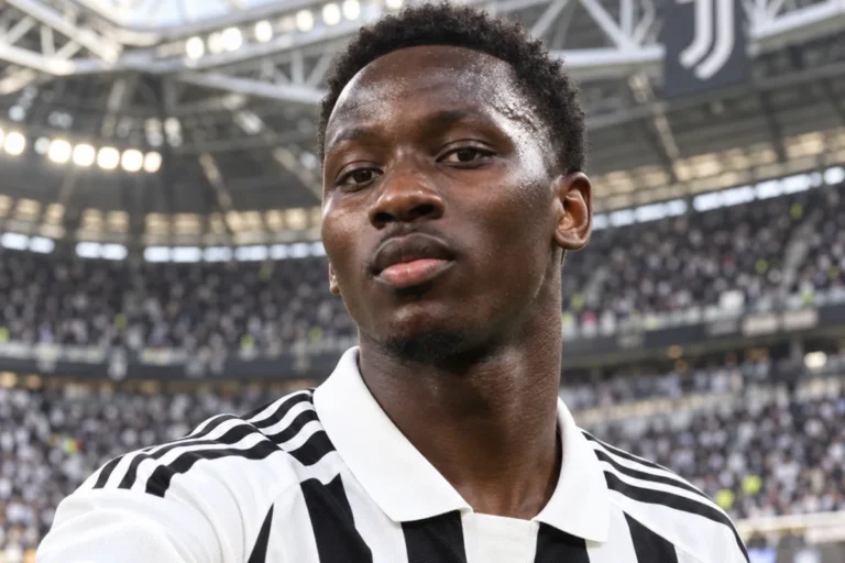 Giocatore della Juventus con maglia bianconera a strisce e colletto bianco, in primo piano durante un selfie in tribuna dello
