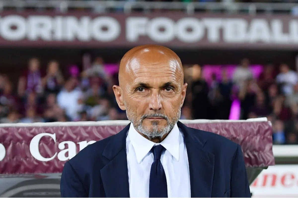 Uomo calvo con pizzetto grigio, giacca blu e cravatta scura davanti a un banner con la scritta Torino Football