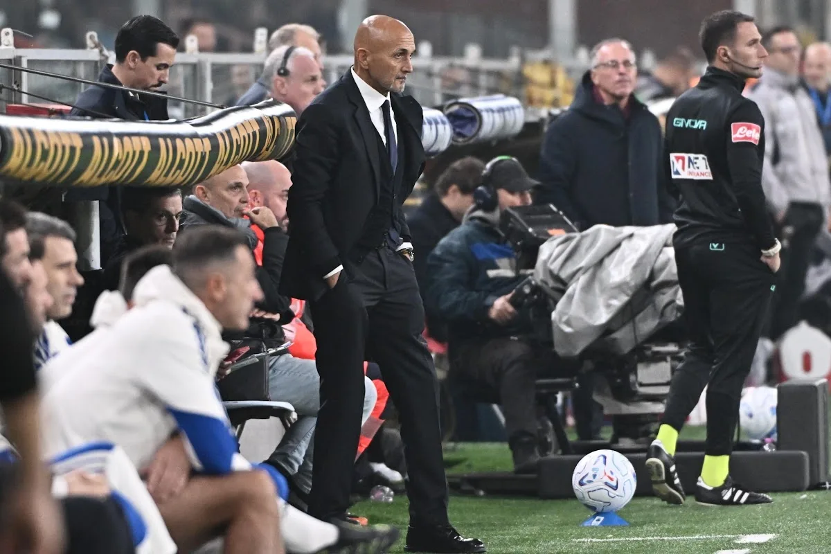 Spalletti in abito scuro a bordocampo durante una partita di calcio, accanto a un pallone sull'erba