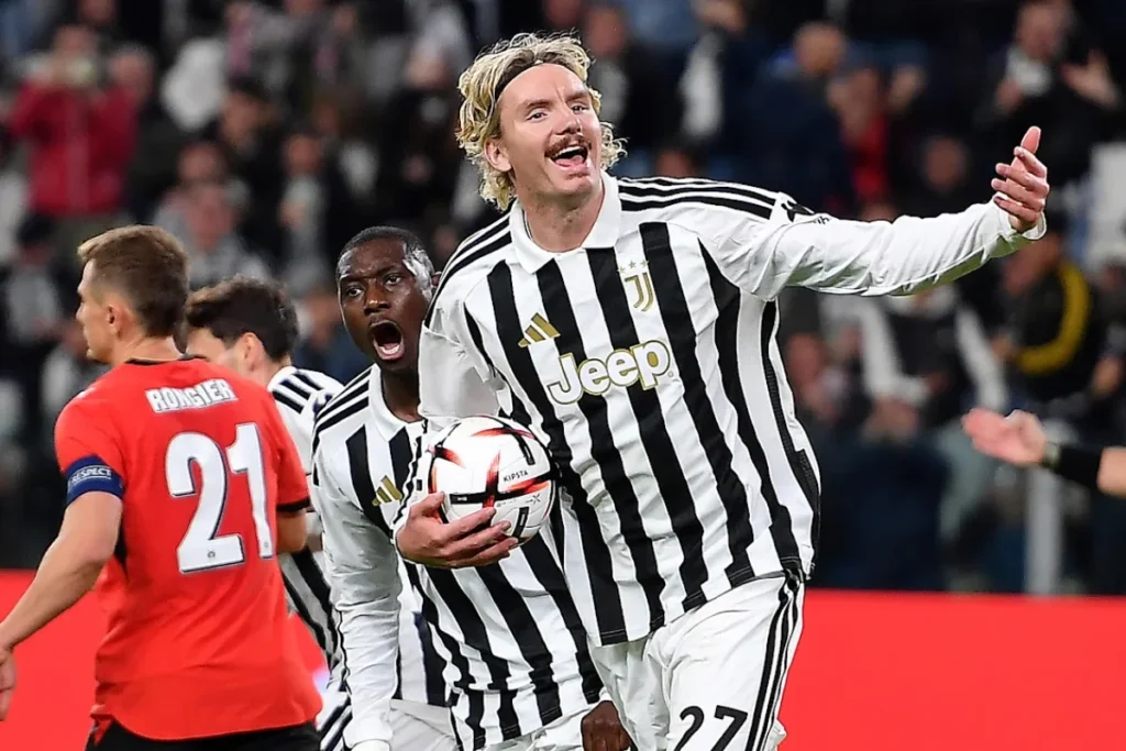 Juventus con maglia numero 27 esulta a braccia aperte in campo, con pallone in mano accanto a un compagno