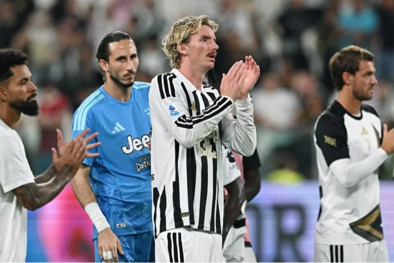Giocatore della Juventus in maglia bianconera con le mani unite durante una partita, circondato da compagni in azzurro e avversari
