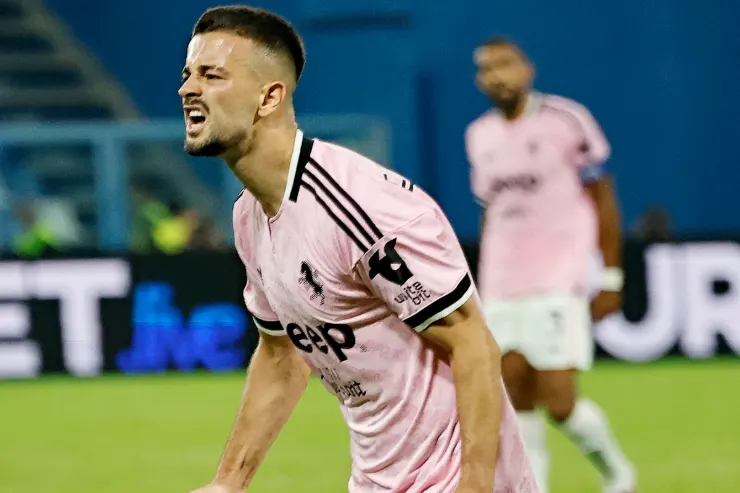 Calciatore della Juventus con la maglia rosa da trasferta esulta a bocca aperta durante una partita serale